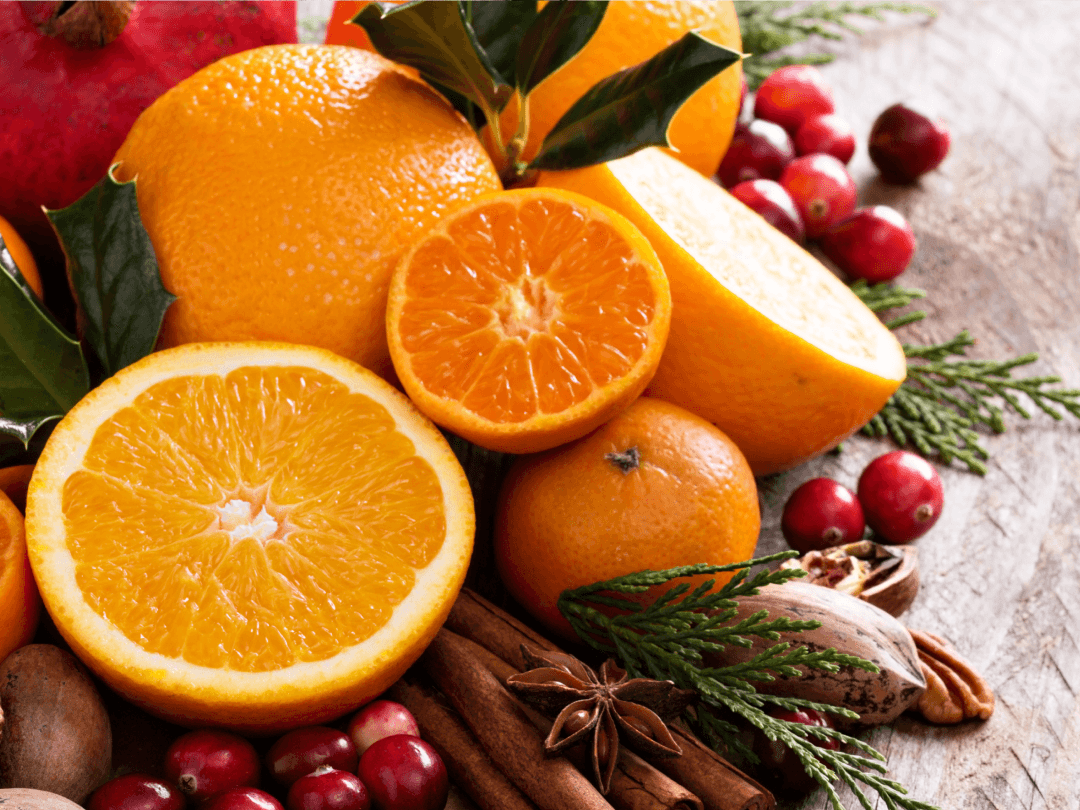 A vibrant arrangement of sliced oranges and tangerines amid cranberries, pine branches, and cinnamon, evoking a festive, cozy atmosphere.
