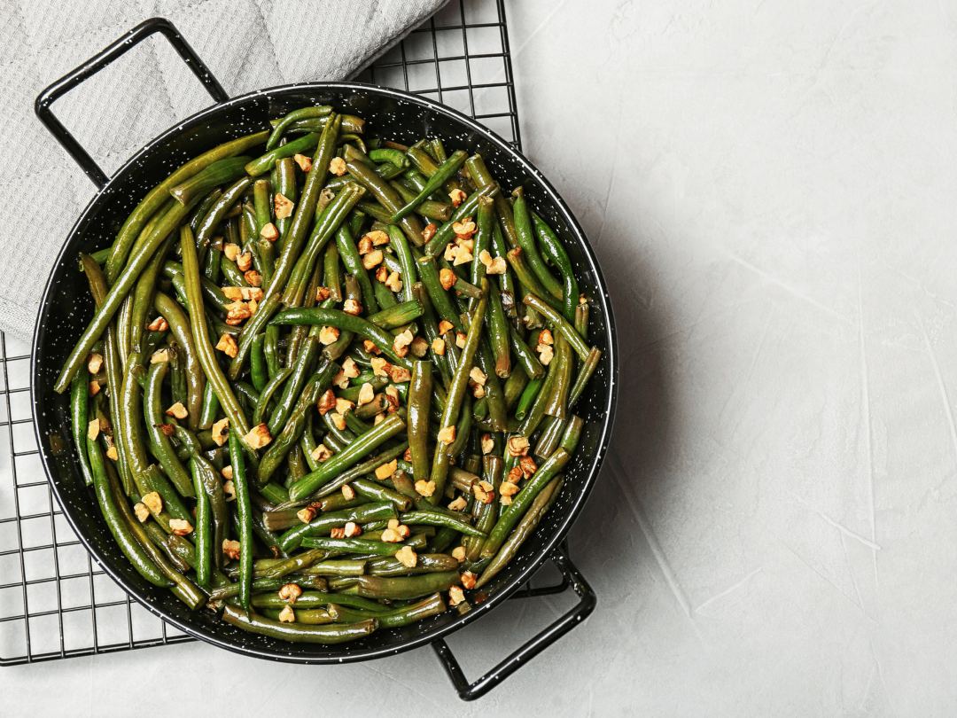 A pan filled with cooked green beans and chopped nuts sits on a cooling rack.